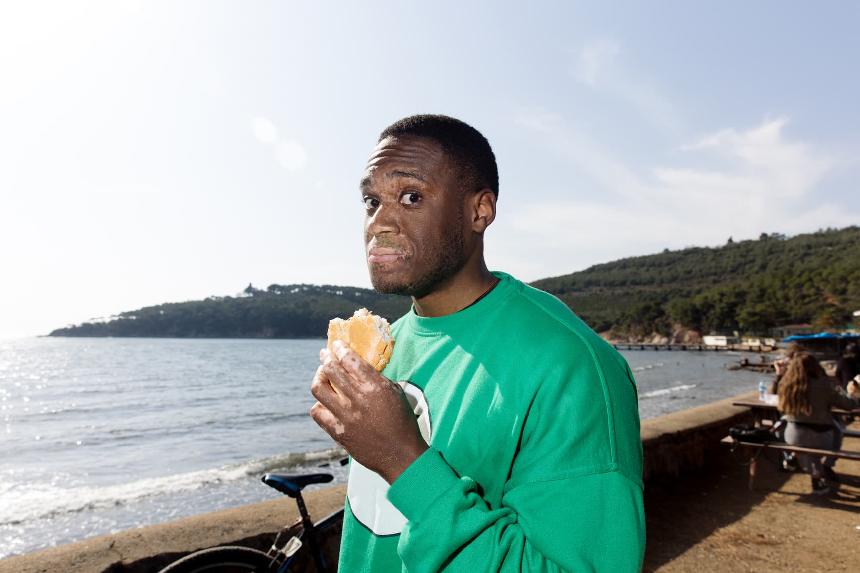 Man holding and eating ice cream near the seaside with a surprised expression, capturing casual outdoor leisure and coastal lifestyle.