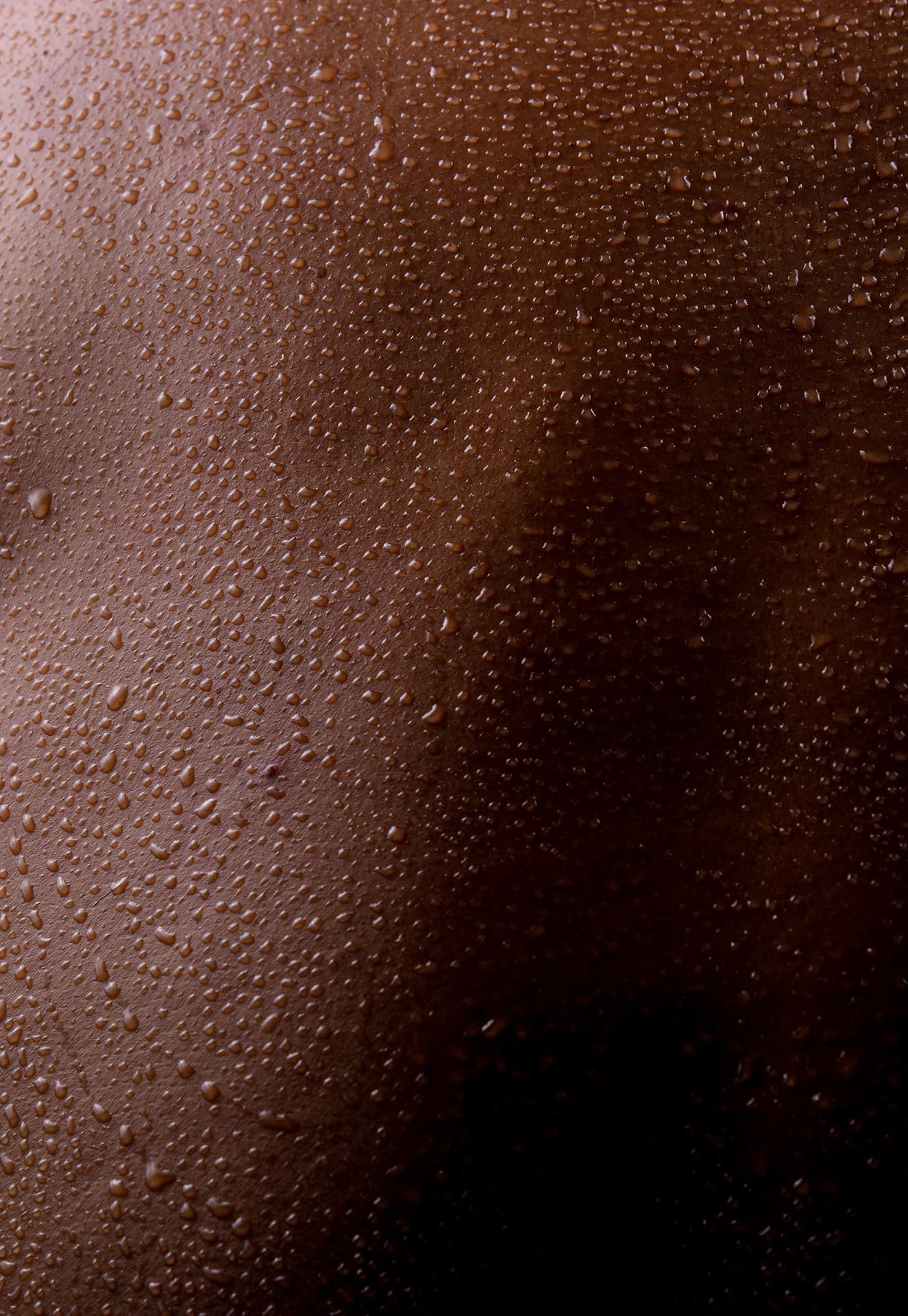 Extreme close-up of dark skin covered in water droplets, highlighting skin texture, hydration, and natural moisture.