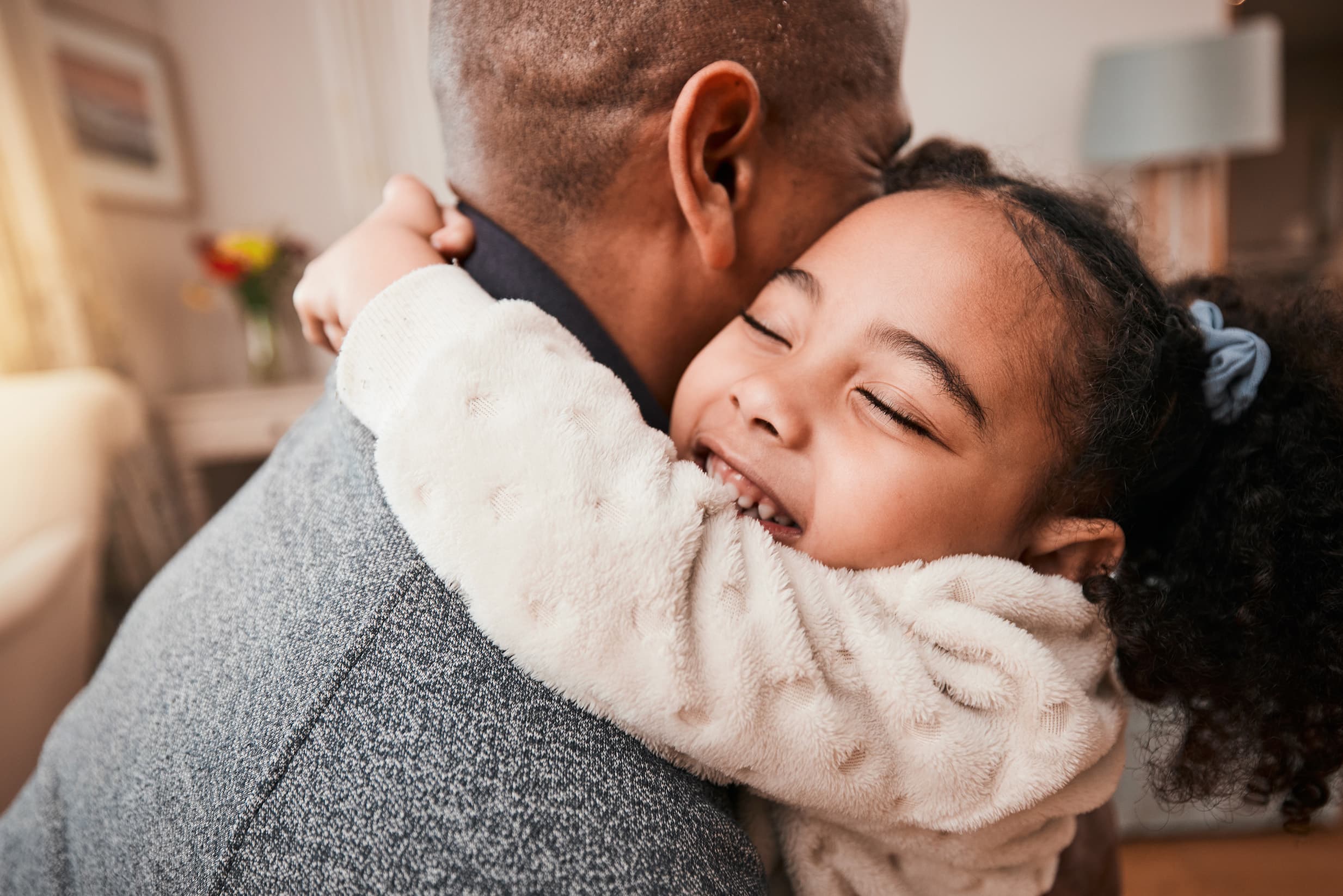 Smiling child hugging an adult indoors, conveying warmth, family connection, and emotional comfort in a home environment.